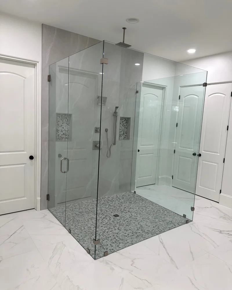 Frameless glass corner shower with a pebble tile floor and white marble-look walls