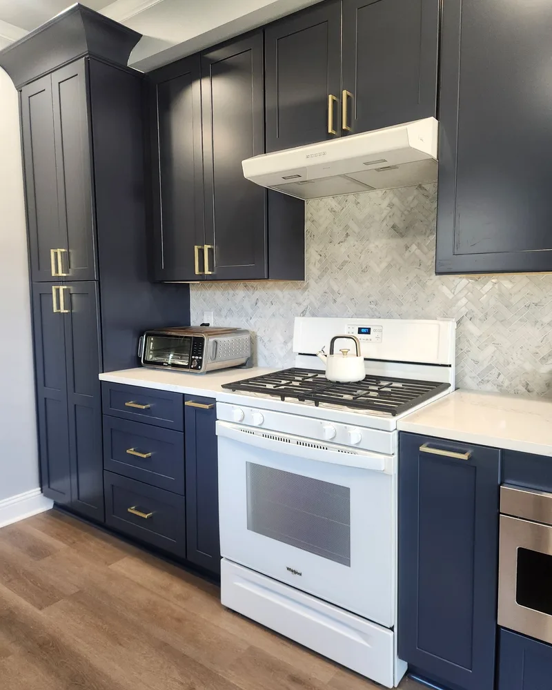Kitchen renovation with navy lower cabinets, a white gas range and a marble-look backsplash