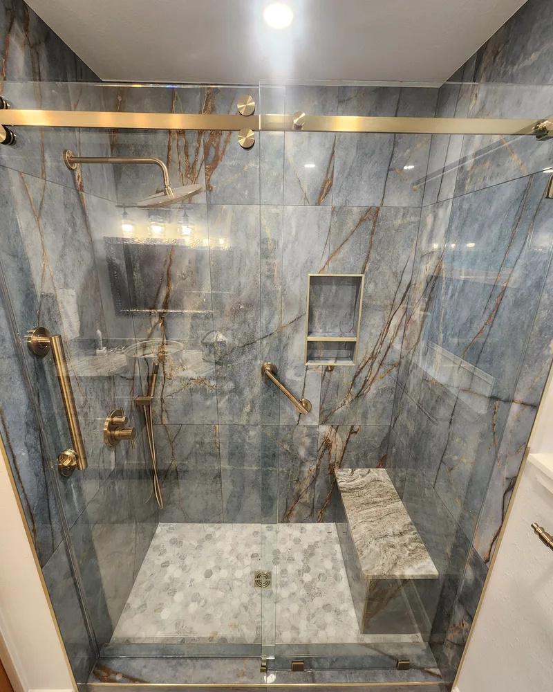 Walk-in shower renovation with gray marble-look slab walls, brushed gold fixtures and a bench