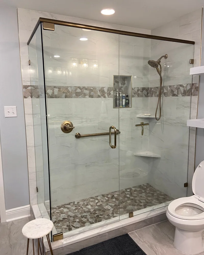 Glass shower with a mosaic accent band, a brass grab bar and a pebble floor
